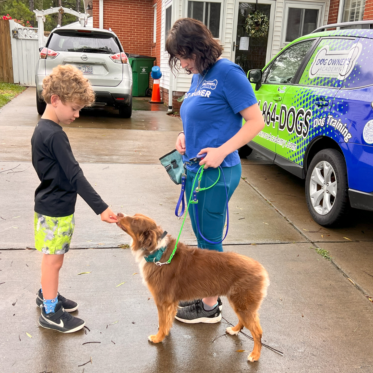 Photo of a dog trainer outside a home with a child giving the dog a treat during lessons